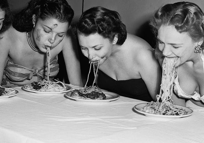 eating fun rivalry women head and shoulders portrait caucasian ethnicity dinner plate competitor flower arrangement spaghetti tablecloth american eating contest swimwear five people new york city table human person food meal dish
